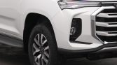 Front left corner of a white pickup truck showing the headlight, grille, and front wheel area.