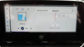 Car touchscreen showing FM radio tuned to 87.6 with play/pause controls and a vertical icon bar on the left side.