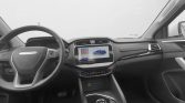 Interior of a modern car cabin with a center touchscreen showing a blue car image and colorful app tiles, plus a rotary gear selector and steering wheel with MAXUS branding.