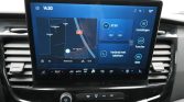 Infotainment touchscreen in a car showing navigation map, radio panel, and right-side quick-access tiles (Settings, Functions, Apps). Climate controls below the screen.