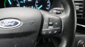 Close-up of a Ford steering wheel showing right-side control buttons; blurred dashboard gauges in the background.