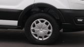 Close-up of a car's front wheel with a silver hubcap and black tire, the white van body in the background