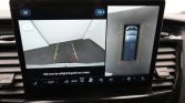 In-car display showing rear camera view with parking guidelines (green/yellow/red) and a top-down vehicle outline with dashed yellow lines around the car for 360-degree guidance.