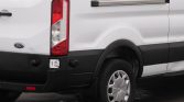 Rear quarter of a white Ford cargo van showing the vertical taillight, black bumper, and wheel arch.