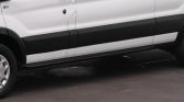 Side view of a white van showing black lower panel, door, and a running board; partial front wheel visible on asphalt surface.