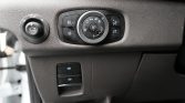 Car interior dashboard showing a circular headlight control dial with fog light buttons and dimmer/brightness controls, plus two vertical switches below for parking brake and auto hold.