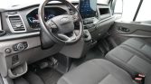 Interior of a Ford van showing the steering wheel, instrument cluster, and large center touchscreen infotainment system in a gray cabin.