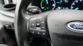 Close-up of a Ford steering wheel showing cruise control buttons on the left side, with the dashboard in the background