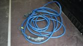 Blue heavy-duty power extension cable coiled on a dark stage floor, with a circular multi-pin connector at one end and a standard plug at the other (informational).