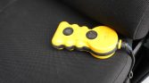 Yellow handheld remote with two black circular buttons on a car seat, connected by a cable to a plug.