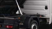 Truck with its flatbed raised by a hydraulic piston, showing the rear chassis and spare components ready for loading or unloading.
