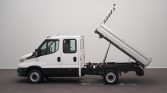 White cab-over truck with a raised hydraulic dump bed, ready to unload on a paved lot
