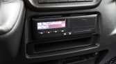 Close-up of a car's center console with an aftermarket diagnostic device; the small screen shows a purple display with status text.