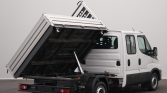 White utility van with its aluminum dump bed raised by a hydraulic cylinder, exposing the rear chassis and tail lights for dumping debris or materials.
