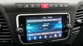 In-car infotainment touchscreen showing FM radio interface with blue graphics, surrounded by control buttons on the dashboard