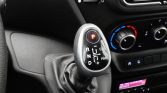 Gear shift lever with PRND plus symbols in a car interior, climate controls visible in the background.