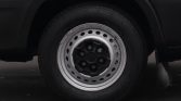 Close-up of a silver steel wheel with circular holes on a dark tire and vehicle body