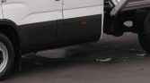 White commercial truck side with black lower body panel and small orange side marker light, on wet pavement beneath a lifted bed edge.