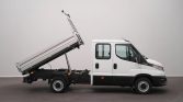White cab-forward utility truck with a hydraulically tilted flatbed raised for dumping cargo (side view).