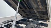 Dump truck bed raised by hydraulic cylinder, exposing the chassis, hydraulic components, and wiring underneath.
