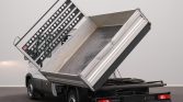 White Iveco Daily dump truck with its cargo bed raised, ready to unload in a clean indoor space.