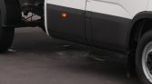 Side view of a white truck with black lower paneling, orange side marker light, and front wheel visible.