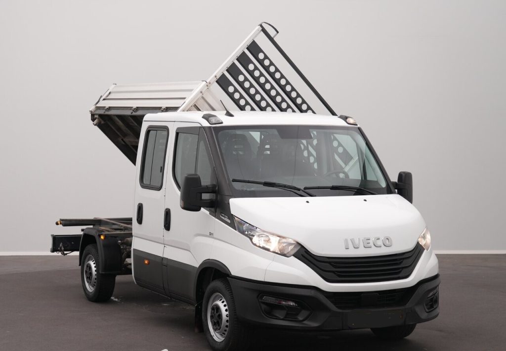 White Iveco dump truck with its tilting cargo bed raised, parked indoors on a gray background.