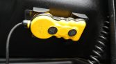 Yellow dual-button remote control pendant with coiled cord mounted on a black surface (likely a vehicle emergency/controls device).