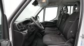 Interior of a white van showing the driver seat, steering wheel, and two passenger seats in the front row, with a dark dashboard.