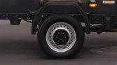 Close-up of a heavy-duty truck wheel: black tire, metal rim, and protective fender against a dark chassis edge
