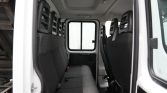 Interior of a white passenger van with gray fabric seats, headrests, and a window at the far end seen from the open side door.