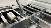 Chassis of a heavy-duty truck with a hydraulic pump and white fluid reservoir mounted in the frame.