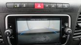 Car dashboard with a touchscreen showing a rearview camera feed and blue guiding lines, warning message in Dutch: 'Volledige omgeving controleren'