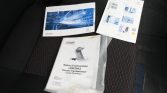 Car manuals and brochures laid on a dark car seat, including a white Peugeot Boxer 'Guide Essentiel' booklet with a blue graphic, plus instruction sheets and a folded envelope labeled 'Notice d'instructions'.