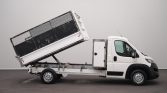 White utility truck with a tilted cargo bed or cage on the back, ready for dumping or loading materials.