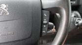 Close-up of a car steering wheel with phone control buttons and a key in the ignition; Peugeot emblem on the airbag.