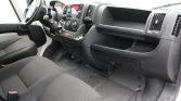 Interior of a van cabin showing steering wheel, dashboard, center console, and front seats with rubber floor mats.
