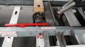 Heavy-duty trailer frame with a small yellow fuel tank, engine, hoses, and a red crossbar; caution labels in French along the frame.