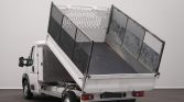White dump truck with its bed raised, exposing a metal cargo bed with mesh side panels for unloading inside a plain room/garage.