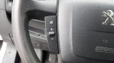Steering wheel of a Peugeot car with left-side control panel showing mute and volume (+/-) buttons.