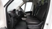 Interior of a white van showing the driver’s seat, steering wheel, and three front passenger seats with black upholstery