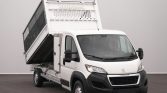 White Peugeot utility truck with its metal dumping bed raised at the back, in a studio setting.