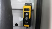 Yellow SPX control pendant with two arrow buttons (up and down) mounted on a vehicle wall for vertical adjustment.