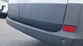 Rear bumper of a gray van with parking sensors and a red reflector on the right side.