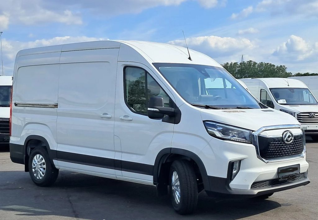Front-left view of a white cargo van with raised roof and black grille, parked in a lot with other vans nearby.