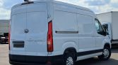 White cargo van parked in a lot, rear and right-side panels visible with tall roof and black bumper edge.