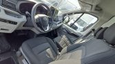 Interior of a van showing the driver’s seat, steering wheel, and a center touchscreen tablet on the dash with grey fabric seats visible.