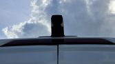 Close-up of a white van roof with a black roof rack mount against a blue sky with clouds, viewed from below.