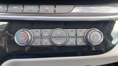 Car climate control panel with left temperature dial (A/C) and right fan-speed dial, row of buttons for airflow and defrosting in a glossy black console.