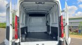 Empty white cargo van with rear doors open, revealing a spacious, bare cargo area with white metal walls and a black rubber floor.